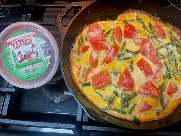 tomato, asparagus and parm cheese frittata in a cast iron skillet with a container of salsa next to it.