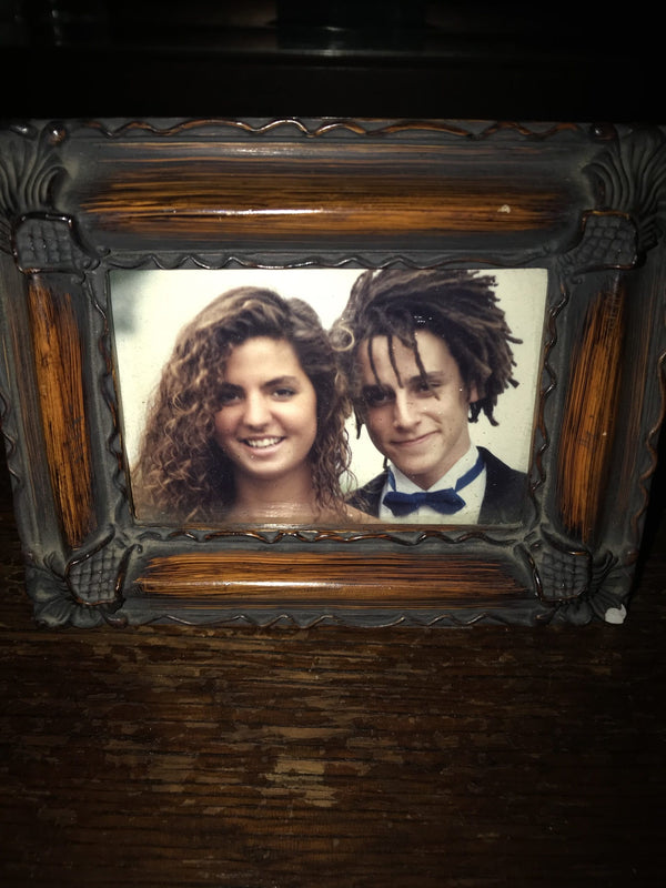 A picture frame with a photo of a young man and woman, him with a tux on, both smiling.