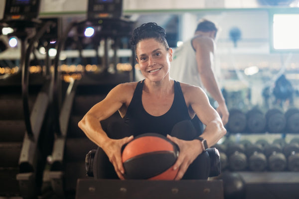 smiling woman in a gym sitting in her workout clothes holding a workout ball